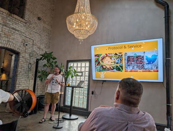A nerd with good arms holding a microphone talking in front of a screen reading "protocol & service"